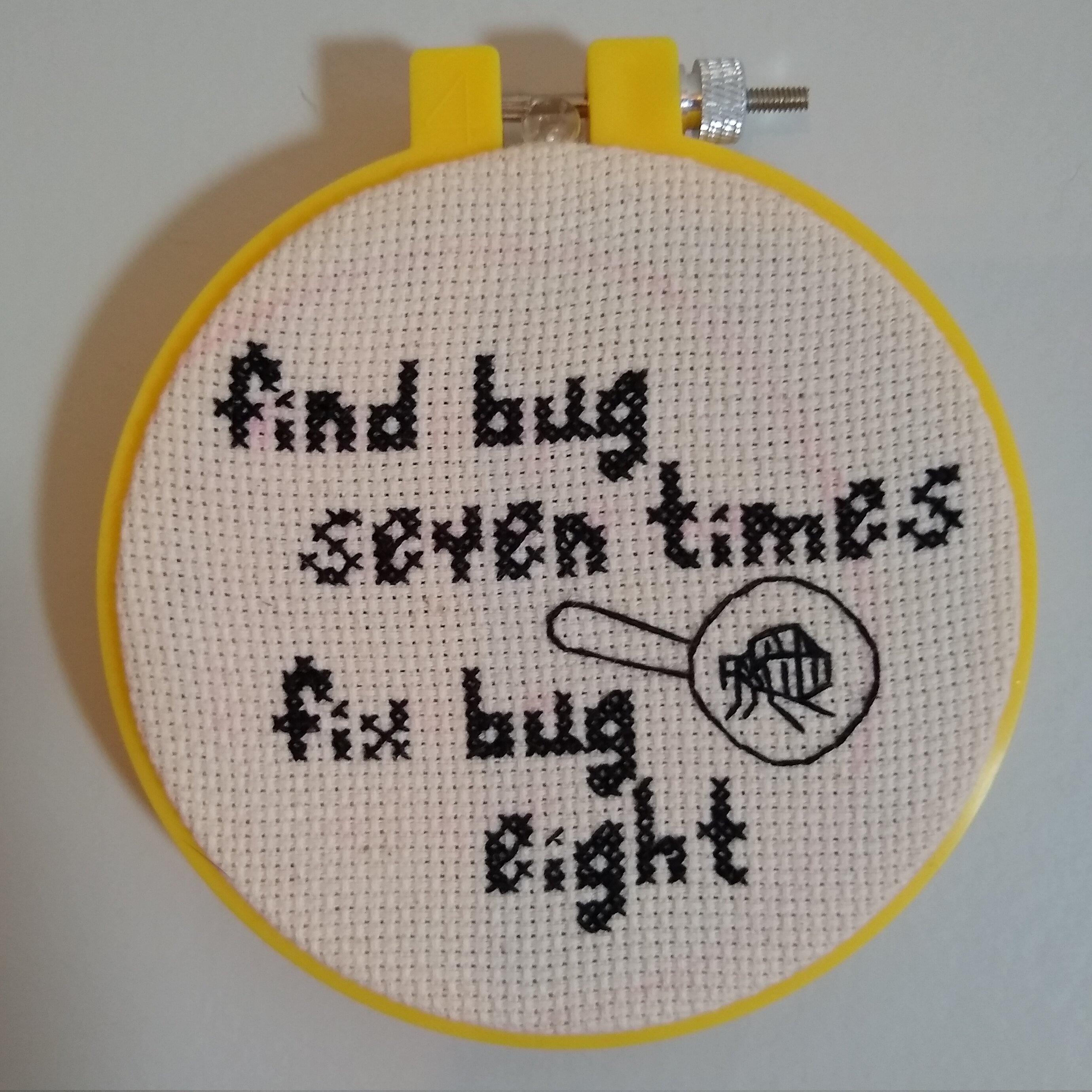 cross-stitch of a flea in a magnifying glass that says 'find bug seven times, fix bug eight'
