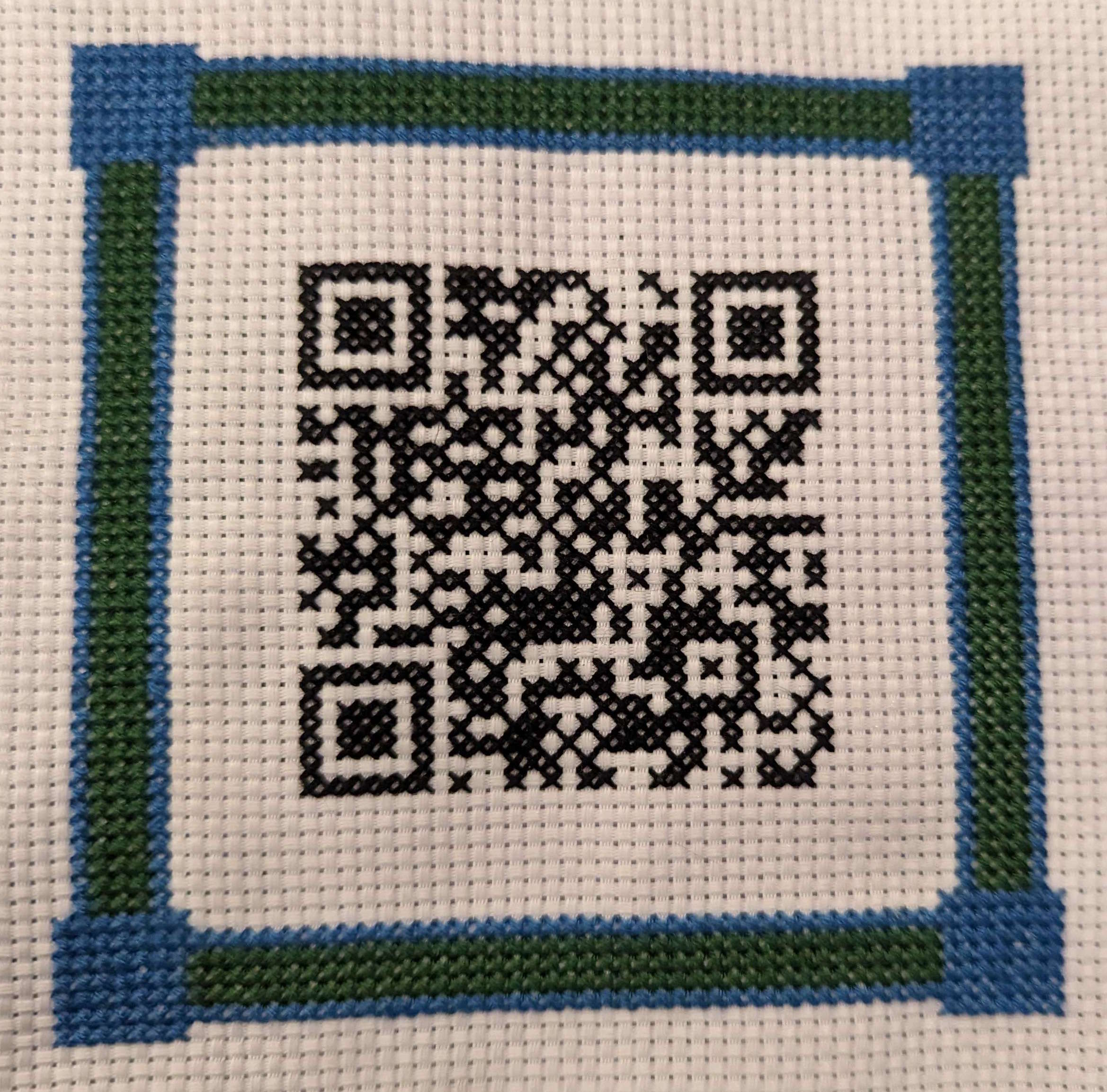 cross-stitch of a QR code of a wifi network and password. The QR code has a solid blue and green decorative border.